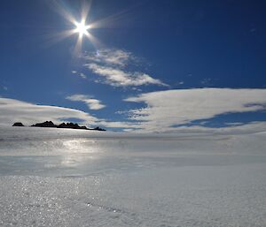 Two men in the distance with lots of ice, some rocks in the distance and clear skies.