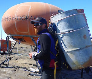 Expeditioner in front of the Béchervaise Island huts with an empty fuel drum on his back.