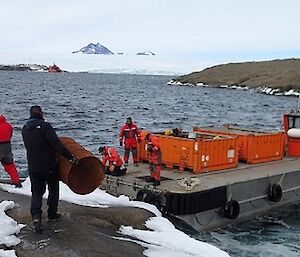 Two men are loading old fuel barrels from an island onto a barge