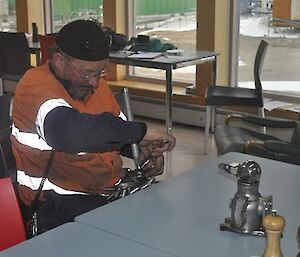A man in a work uniform holds a spanner and is making a metal Echidna