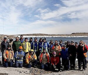 A group of 24 expeditioners wearing winter coats stand in front of the harbour