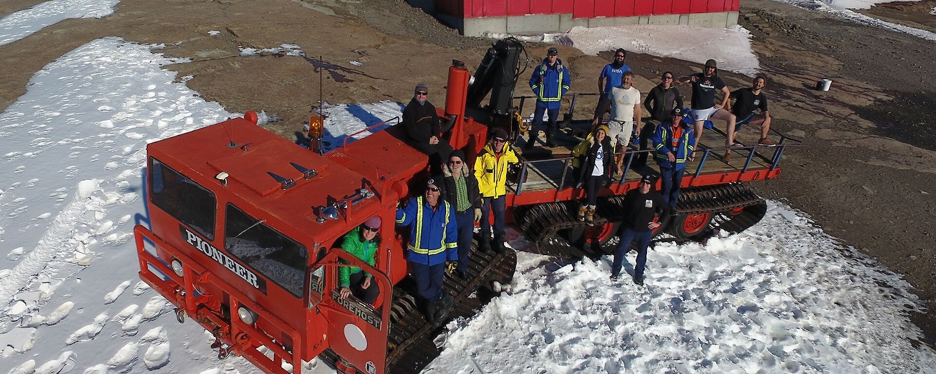 A large red over snow vehicle holding 14 expeditioners is parked in front of the Mawson living quarters