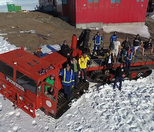 A large red over snow vehicle holding 14 expeditioners is parked in front of the Mawson living quarters