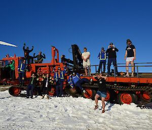 A team of expeditioners are posing on a red over snow vehicle for a group shot