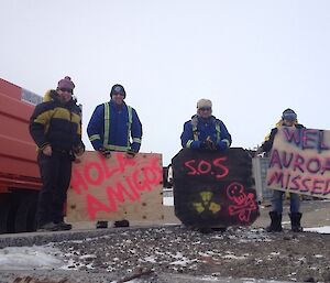 Five expeditioners are holding hand made signs that read “Hola Amigos”, “SOS”, “Welcome Aurorra V3.2 Missed U 2”