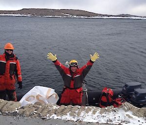 two men in red suits are standing in a twin engine boat holding their arms up in the air