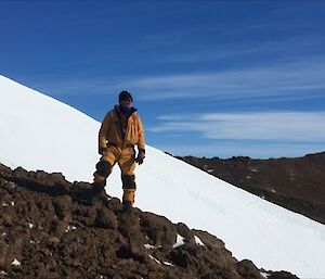 a man in a yellow snow suit stands on a mountain