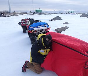 A man kneeling down by a quad bike setting up a bivvy