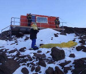 Some expeditioners standing outside a hut looking for a good spot to put up a bivvy bag.