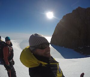 three expeditioners stand on an ice ridge with the sun shining