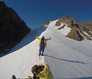 an expeditioner stands on an ice ridge with arms outstretched