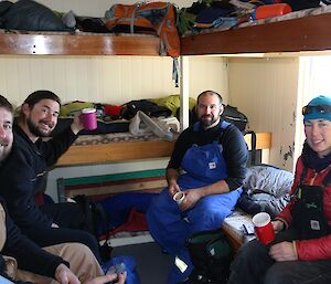 Four expeditioners are having a cup of coffee inside a field hut
