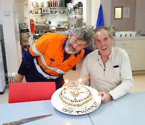 two men pose in front of a birthday cake