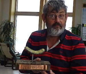 a man holds a golden sausage cast from lead on a wooden stand