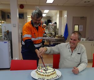 two men cut a round birthday cake together