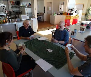 four people sit around a table playing a game of cards