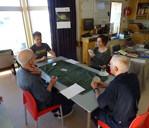 four people sit around a table playing a card game