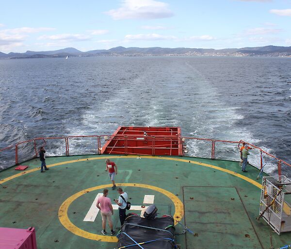 Five people stand on a helideck at the rear of a ship