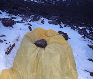a yellow bag is being held down by two rocks on ice