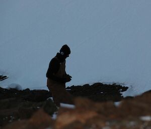 a man in a beanie is walking on some rocks