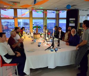 Thirteen people sit around a decorated table while a chef is talking to them