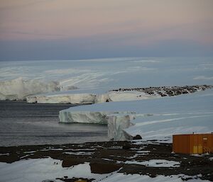 a view of a peninsula with ice cliffs at dusk; and a small red hut in the foreground