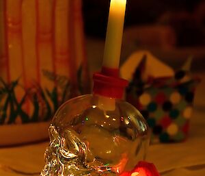 a glass skeleton head holds a candle with a red illuminated flower on a table