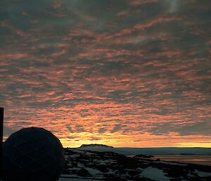 A pink and yellow sunset with a building and a dome in the foreground and a mountain range in the distance