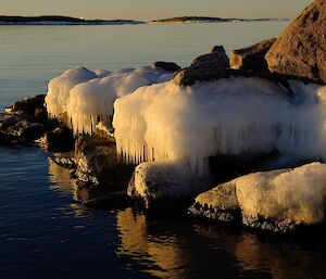 White icicles are hanging over the waters edge off rocks on a harbour at sunset