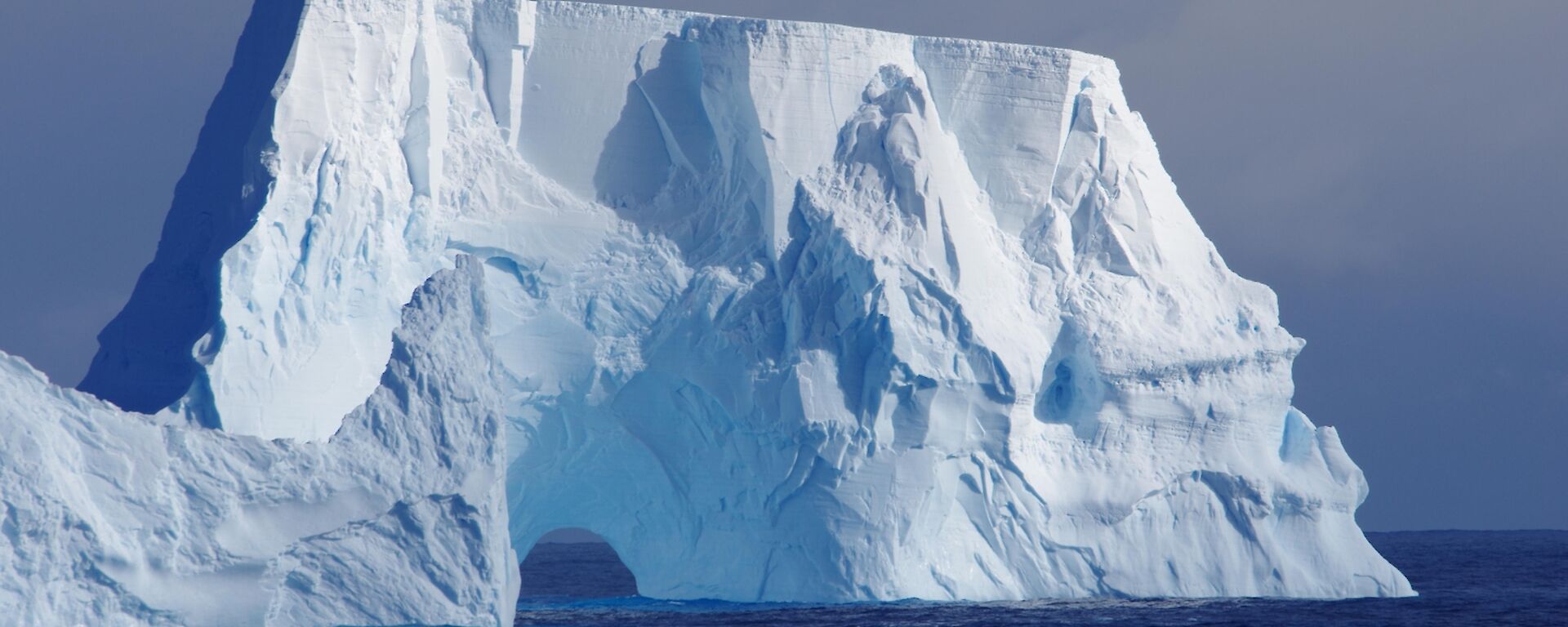 an iceberg with an arch carved out of it looks like a bridge on the southern ocean