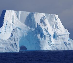 an iceberg with an arch carved out of it looks like a bridge on the southern ocean