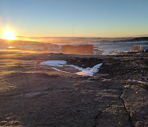 light snow drifts across rock while the sunsets over mawson station