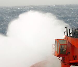The red bow of the Aurora Australis impacts a wave on the southern ocean