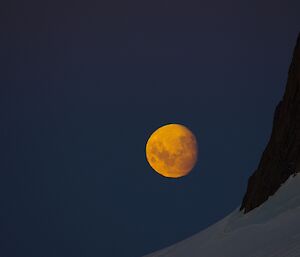 an almost yellow full moon rises alongside the Rumdoodle mountain range