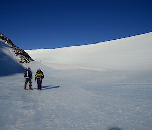 a man and a woman are standing on an icy plateau with a blue sky