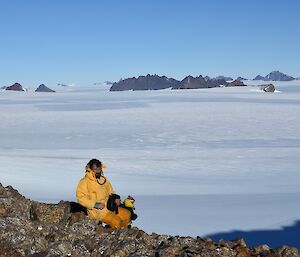 a man in a yellow outfit sits on rocks overlooking a plateau