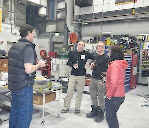 four people stand in circle talking in a workshop