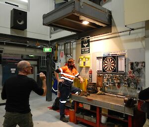 A man throws a dart while two men watch