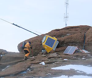 A man in a yellow snow suit inspects fallen radio components on a rocky mountain