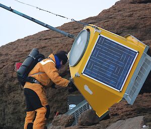 A man in a yellow suit inspects the yellow receiver hanging against rocks