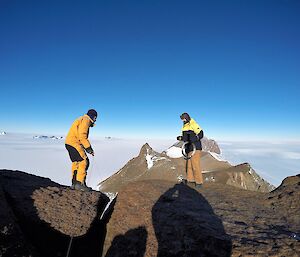 Two men stand on a mountain edge holding cable wire in their hands