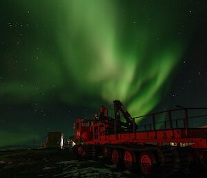 A red truck is in the foreground with a green aurora in the night sky