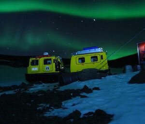 Bands of green auroras behind the yellow Hägglunds vehicle at Fang Hut