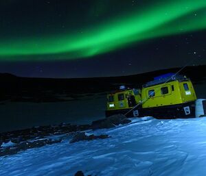 A green band of auroral ribbon with a yellow Hägglunds in the foreground