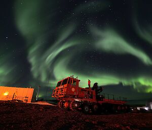 Auroral ribbons of white and green fall above the red Pioneer truck