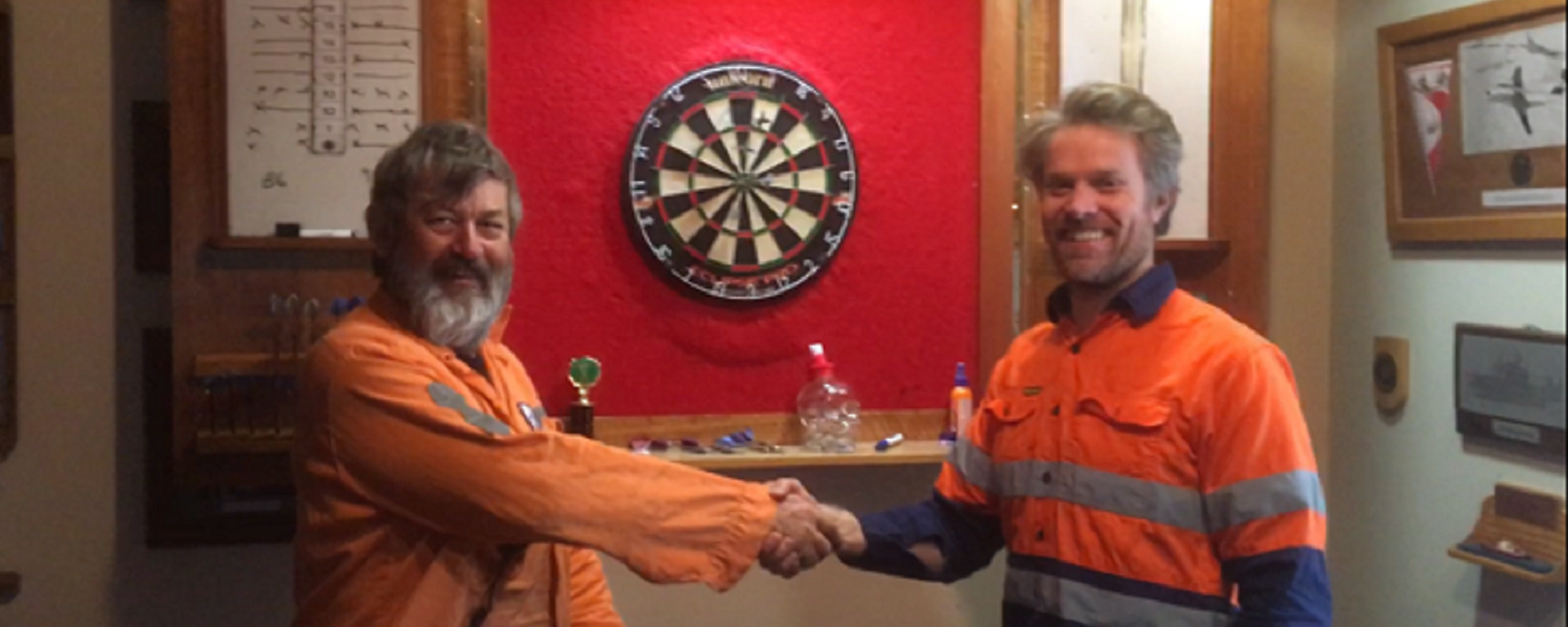 two men stand in front of a dart board shaking hands