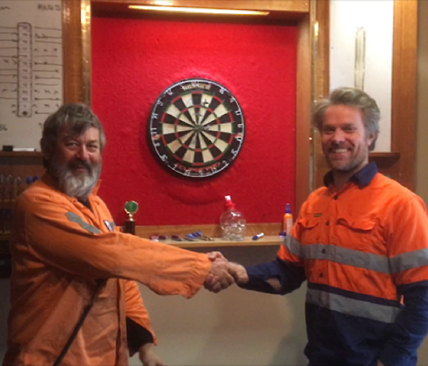 two men stand in front of a dart board shaking hands