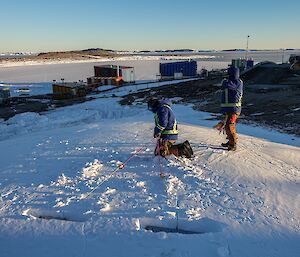 two men set up snow anchors in a mound of ice and snow