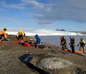 a team of six people in harnesses and helmets set up rescue ropes on a rocky edge