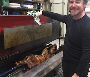 a man stands in front of a lamb on a spit roast